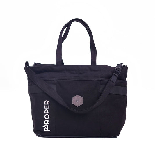 A black tote bag with the text 'PROPER' on the side, featuring a large main compartment, a front pocket, and adjustable straps.