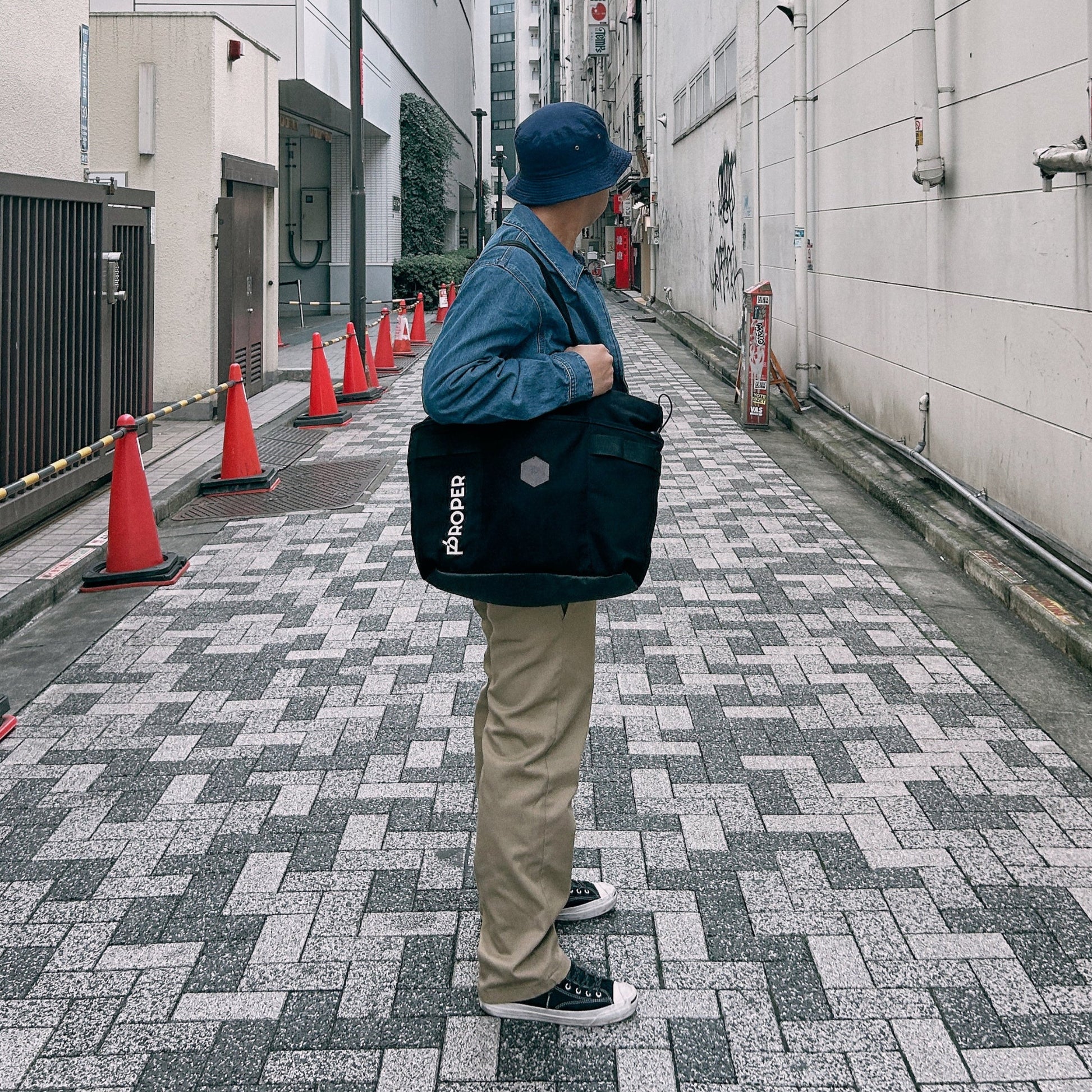 Person holding a black tote bag with visible branding on a city street.