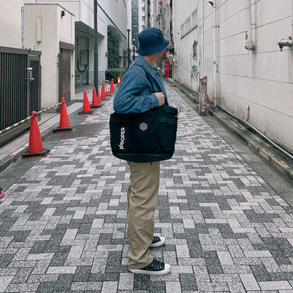 Person holding a black tote bag with visible branding on a city street.