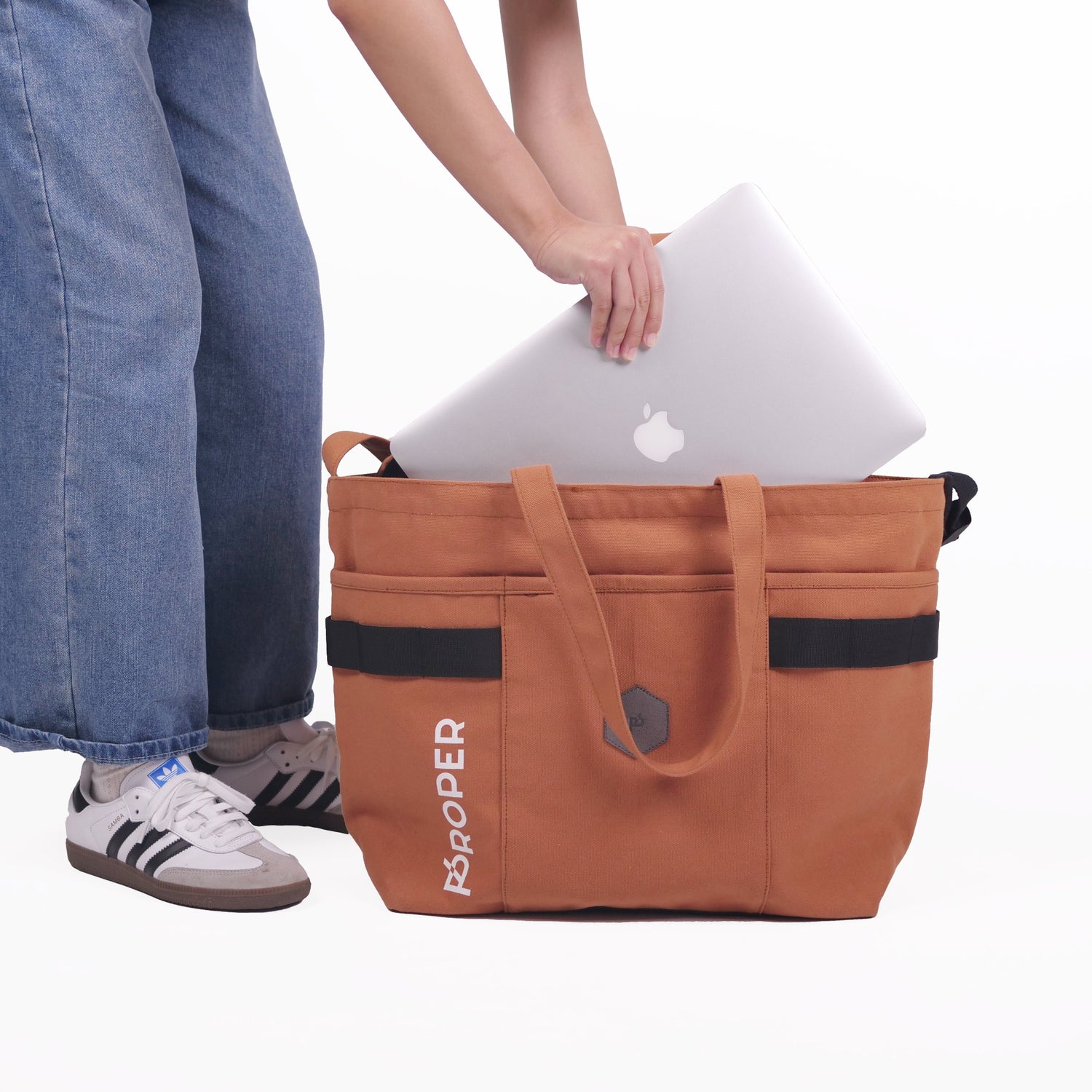 A thai tea color big tote bag with the text 'PROPER' on the side, featuring a large main compartment, a front pocket, and adjustable straps.